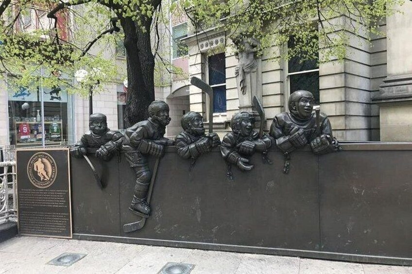 A bronze sculpture of four figures leaning on a wall, with a plaque to the left. 4