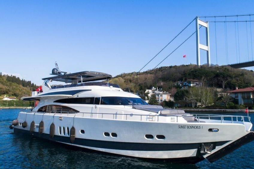 A large yacht named 'SULTAN BOYUKUS' docked near a bridge with a mountainous backdrop. 1