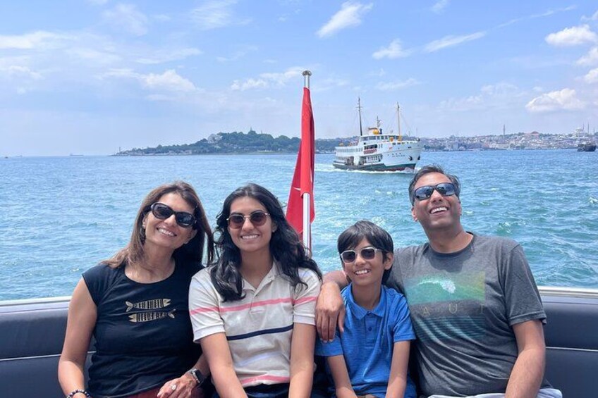 Un groupe de personnes se trouve sur un bateau, avec un drapeau, de l’eau et une côte visible au loin. 4