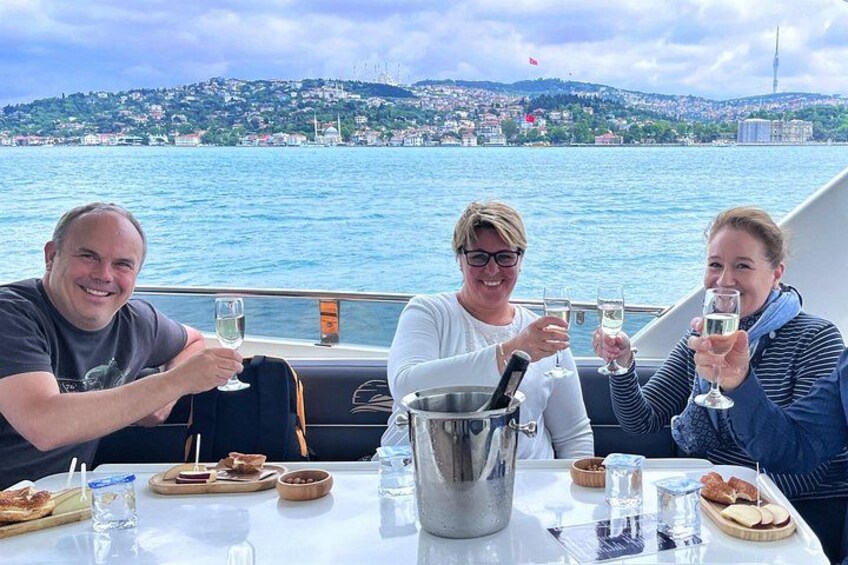 Trois personnes trinquent avec des coupes de champagne sur un bateau, avec une vue sur la ville en arrière-plan. 3