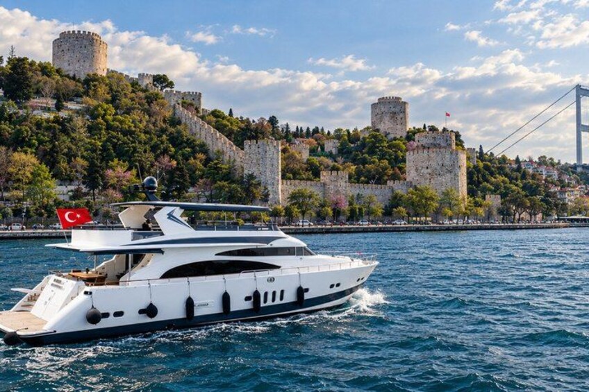 Un yacht blanc, arborant un drapeau turc, navigue sur une étendue d’eau. On aperçoit, en arrière-plan, un château et un pont. 5