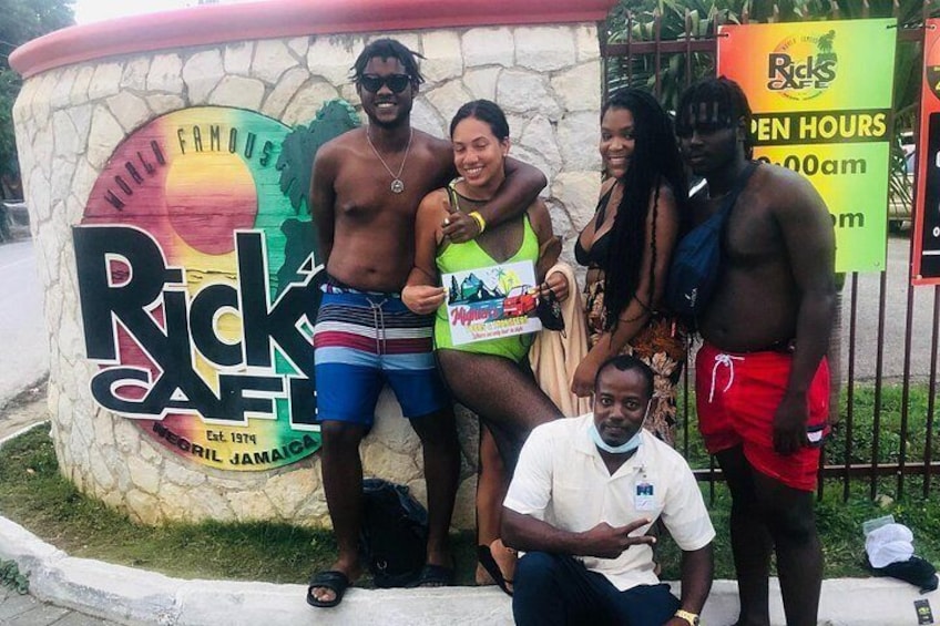 Un gruppo di persone che posa davanti al cartello del Rick's Cafe, un rinomato ristorante giamaicano. 1
