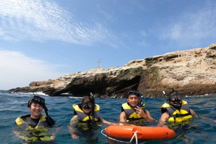 Four people in the water with scuba gear, a rocky coastline, and a lifebuoy. 4