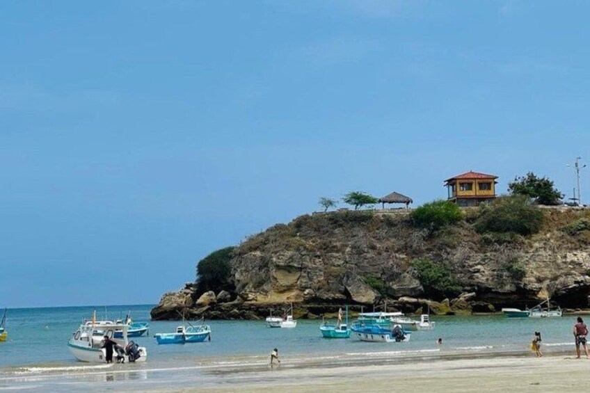 A beach with boats, a rocky cliff, and a small building on top. 2