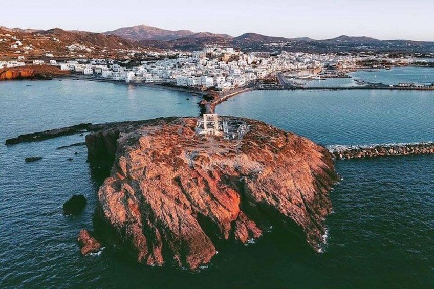 A coastal town with white buildings, a rocky island, and a clear blue sea. 1