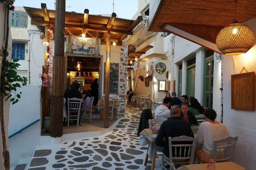 A narrow street with outdoor seating, a café, and a stone wall. 2
