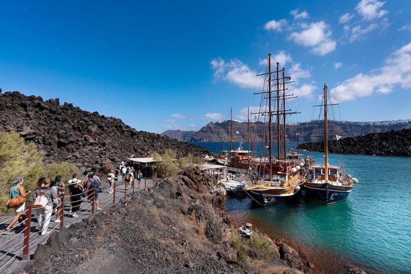A coastal area with people walking along a path, boats docked in the water, and a rocky landscape with mountains in the background. 5