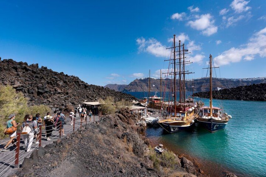 A coastal area with people walking along a path, boats docked near the shore, and a mountainous backdrop. 3
