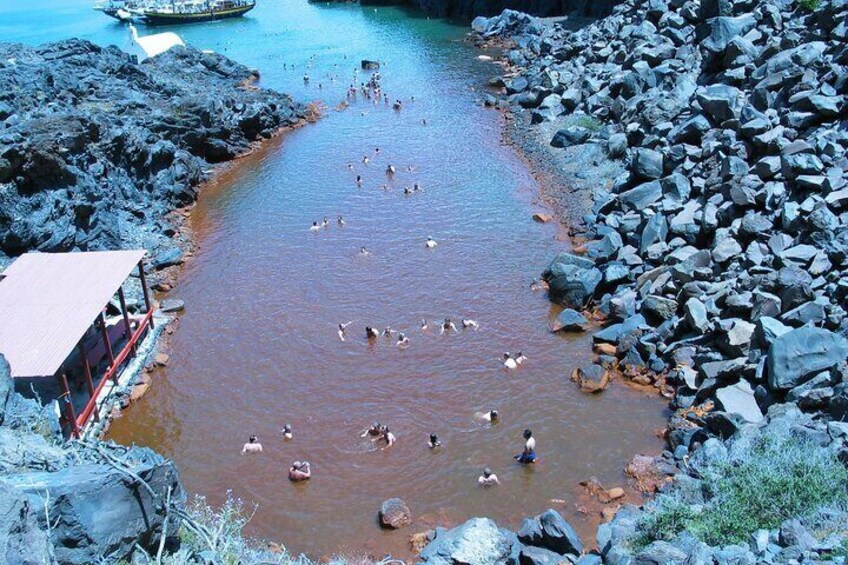 A rocky riverbank with people swimming and a boat in the water. 3