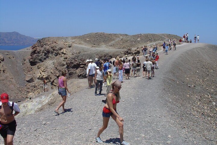 A group of people walking on a rocky path with a view of the sea and mountains in the background. 5
