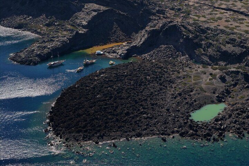 An aerial view of a rocky coastline with clear blue waters, boats, and a small green lagoon. 2