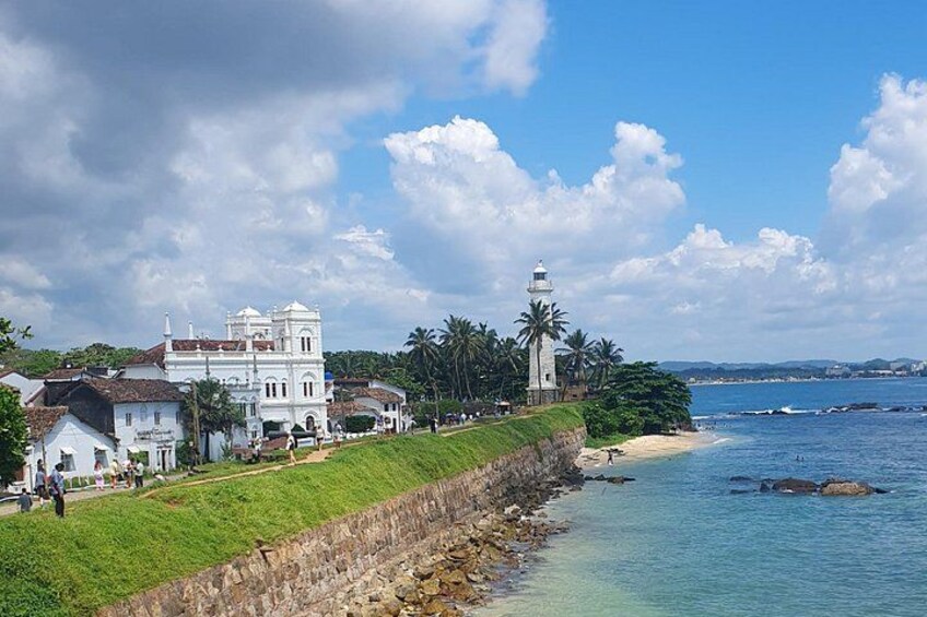 A coastal town with a prominent white building, a lighthouse, and a beach. 5