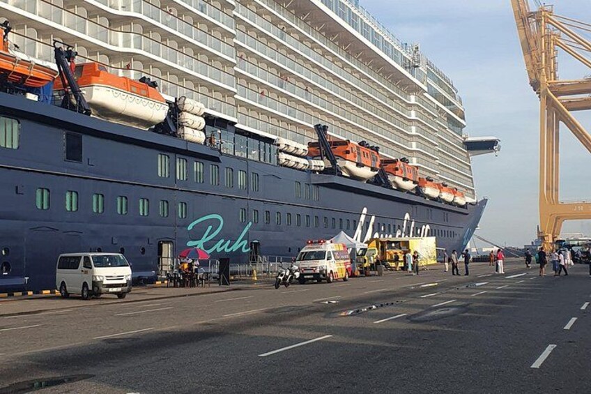 A large cruise ship docked at a port with a crane and several vehicles nearby. 2