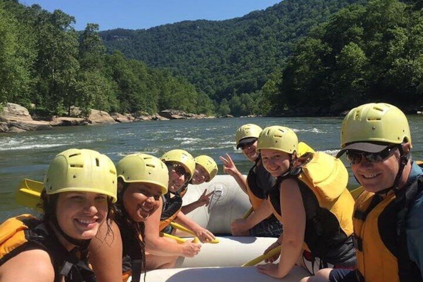Een groep mensen die op een raft een rivier afdaalt, omringd door beboste heuvels. 1