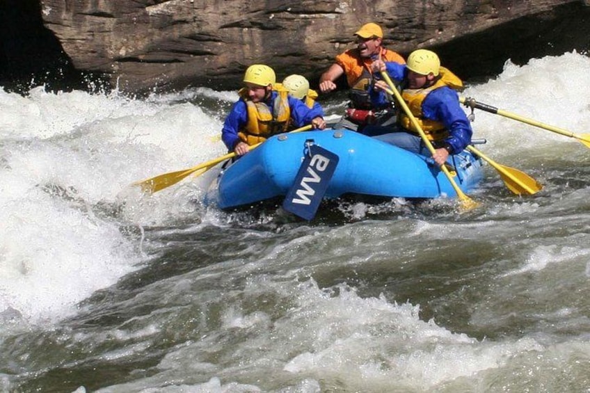 A group of people in a blue inflatable raft navigating through white water rapids. 3