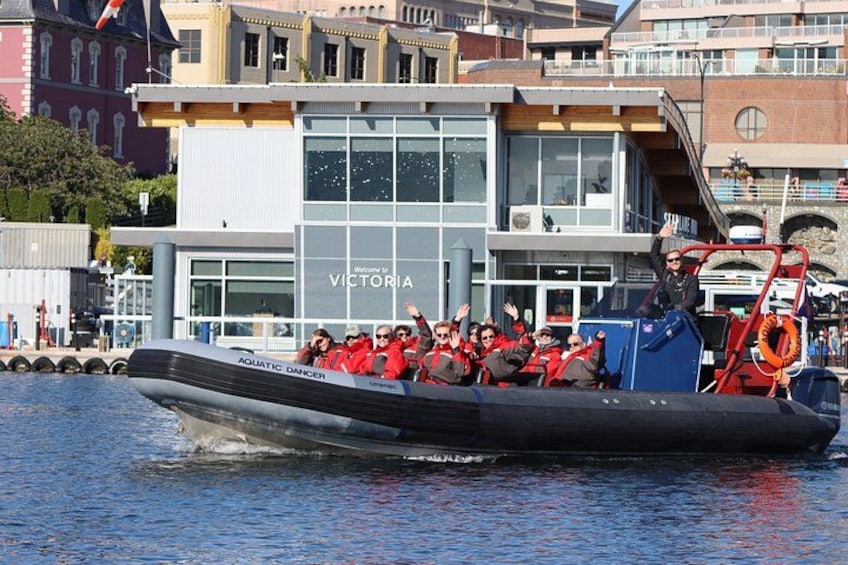 A boat with people wearing red life jackets, a building with 'Victoria' on it, and a dock in the background. 1