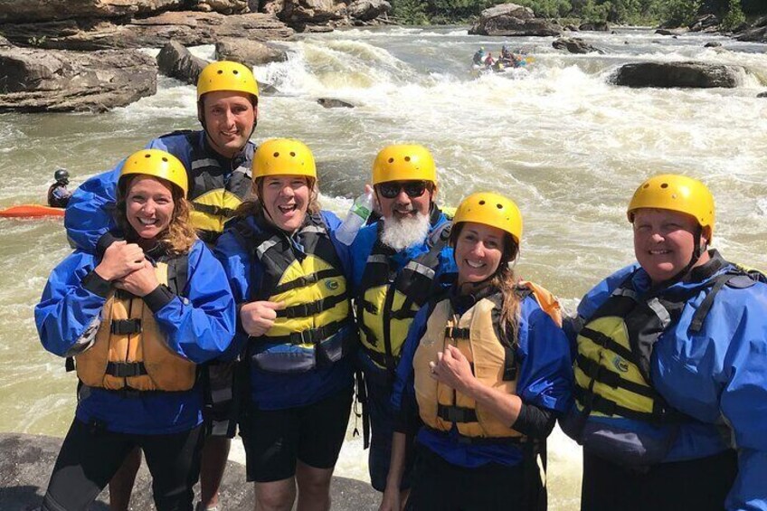 Een groep mensen met helmen en reddingsvesten staat langs een rivier met watervallen. 3
