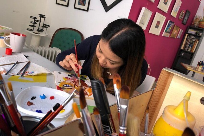 A person painting at a table with various brushes and paint containers. 1