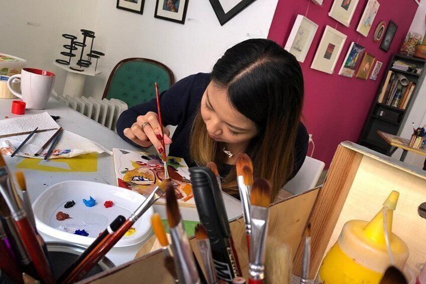 A person painting at a table with brushes, paint, and a palette. 1