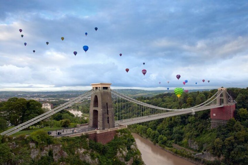 A suspension bridge with hot air balloons in the sky. 1