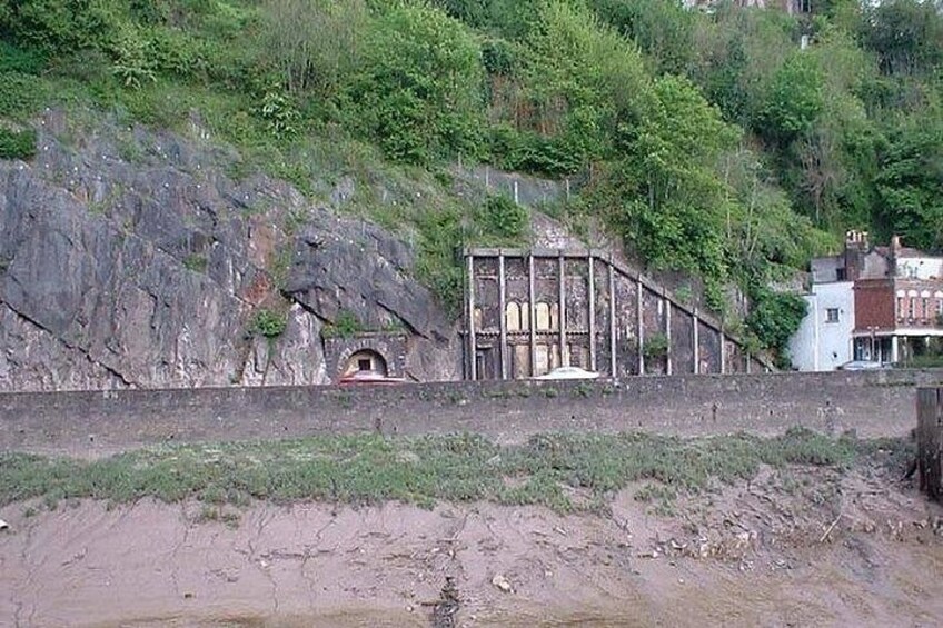 A rocky hillside with a cave entrance, a wooden structure, and a building in the background. 3