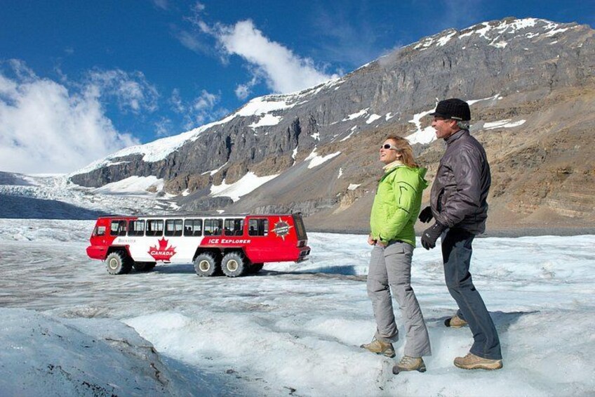 A red and white bus labeled 'ICE Explorer' on a glacier with a mountainous backdrop. 5