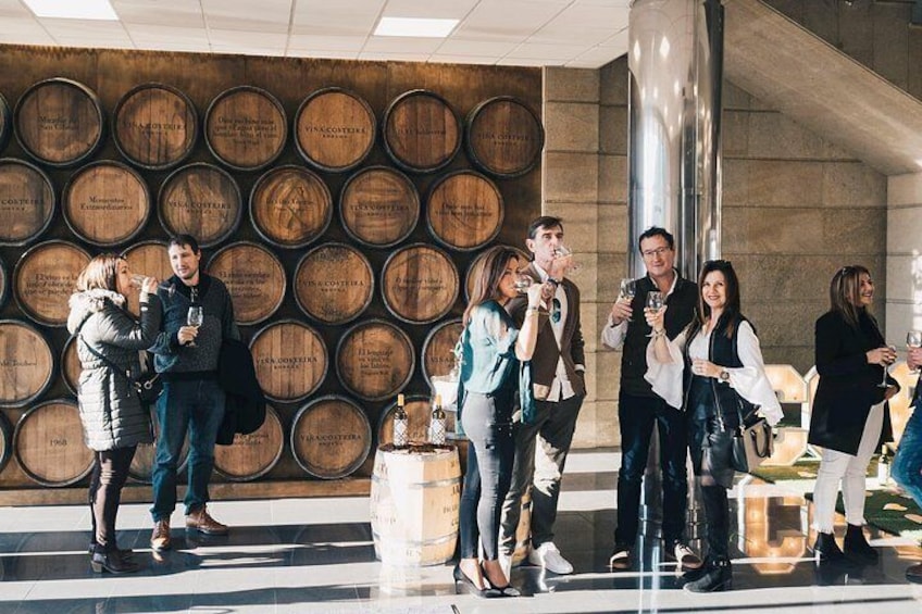 Un groupe de personnes se tient devant un mur composé de barils en bois, et certaines d’entre elles tiennent des verres à la main. 3