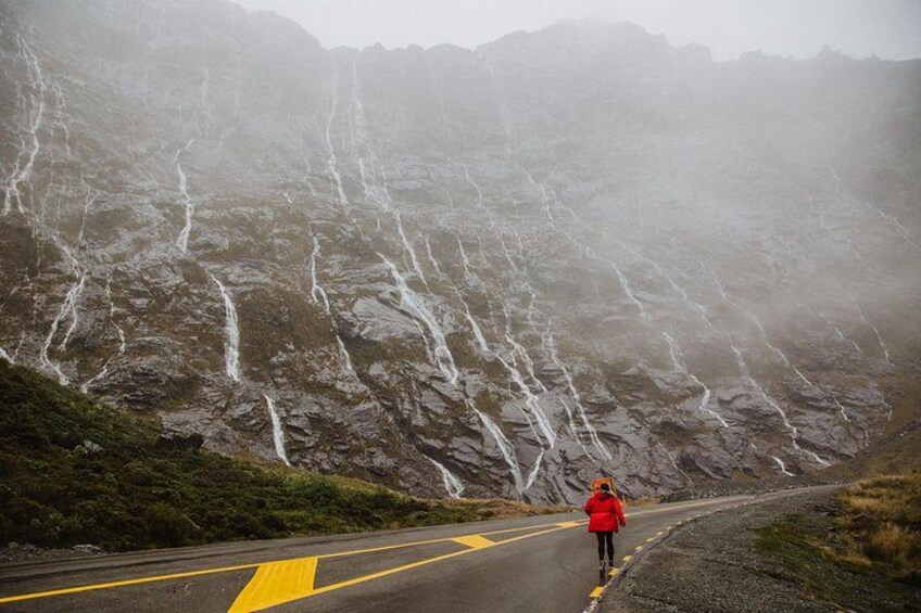 A person in a red jacket walking on a road with a mountain in the background. 5