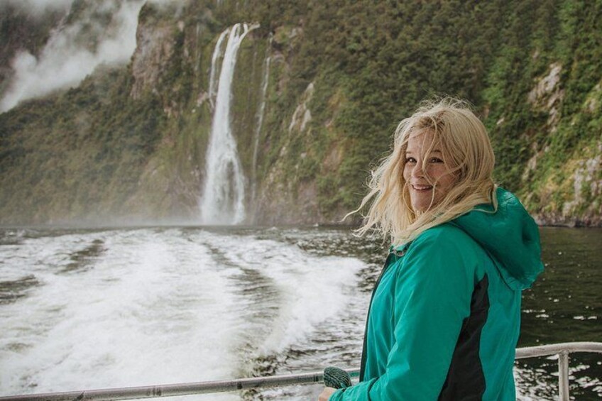 A person in a green jacket standing on a boat with a waterfall in the background. 4