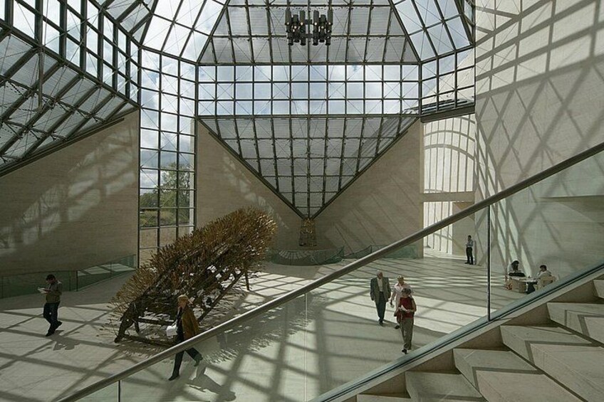 A spacious interior with a glass ceiling, a central sculpture, and a staircase. 3
