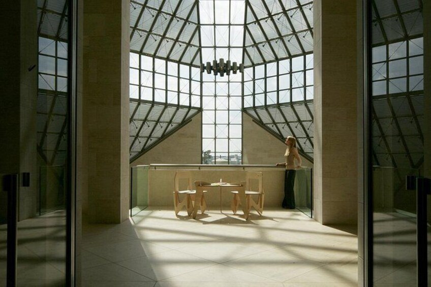A modern interior with a glass ceiling, a table with chairs, and a person standing by the window. 2