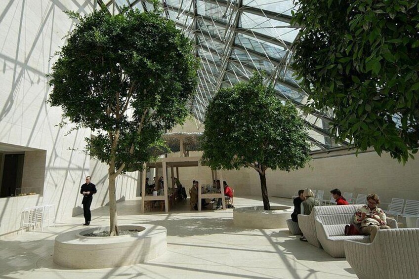 An indoor atrium with a glass ceiling, two trees, and seating areas. 2