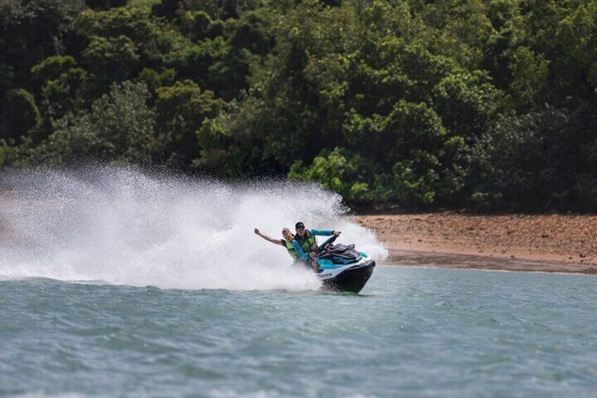 A person riding a jet ski on water with a forested shoreline in the background. 3