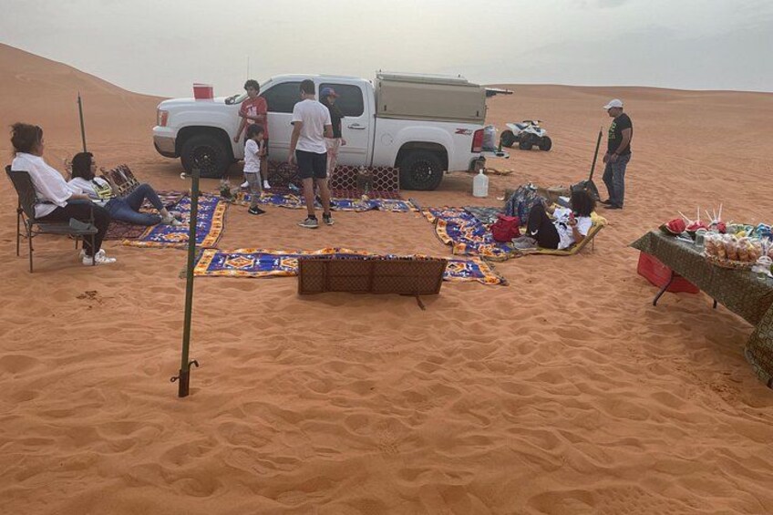 A desert scene with people, a truck, and a table with food. 4