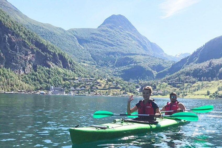 Twee mensen kajakken op een rustig meer, omgeven door bergen. 2