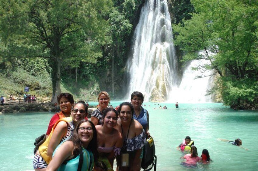 A group of people near a waterfall in a forested area with clear water. 2