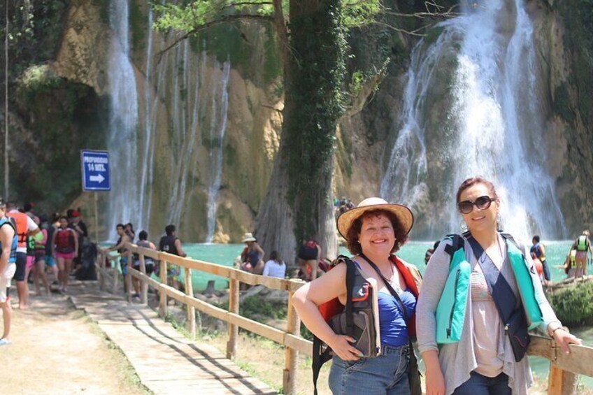 A group of people on a wooden bridge with a waterfall in the background. 3