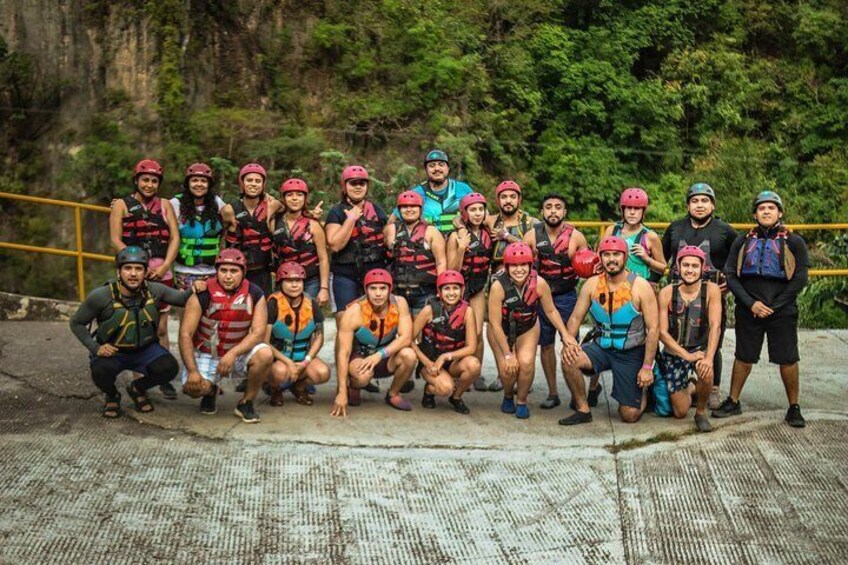 A group of people in helmets and life vests posing for a photo on a concrete surface with greenery in the background. 1