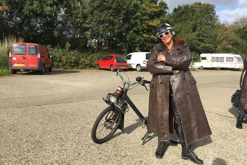 A person standing next to a bicycle in a parking lot with vehicles and trees in the background. 1