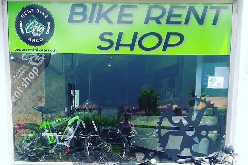A bike rental shop with a green sign, bicycles inside, and a person standing by the window. 1