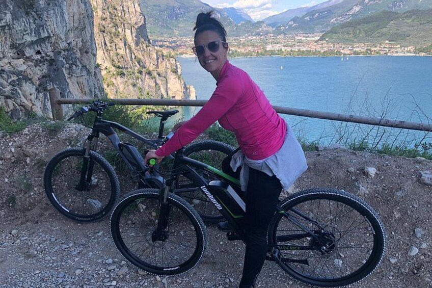 A person leaning on a mountain bike with a scenic lake and cliffs in the background. 2