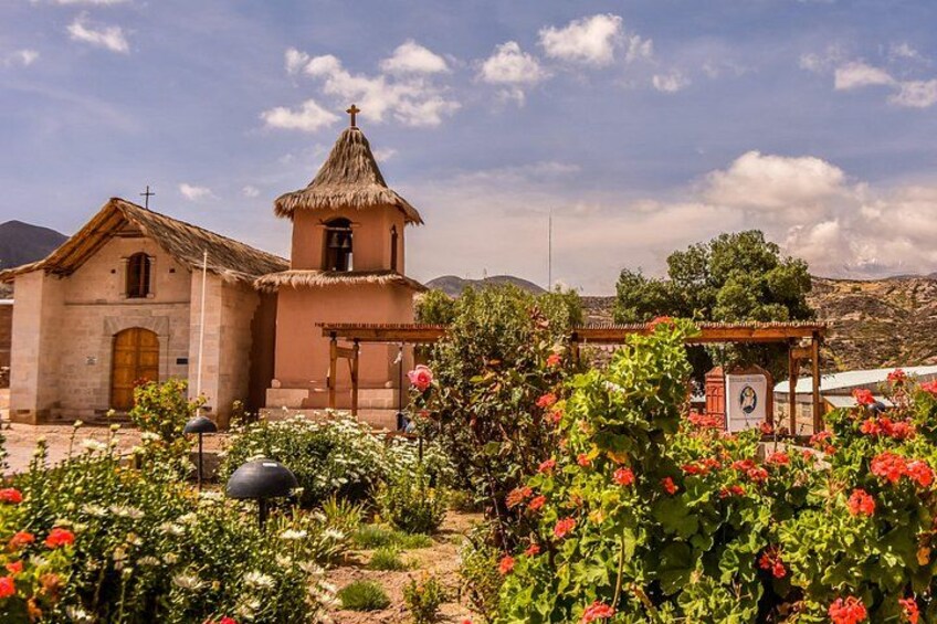 A church with a thatched roof, surrounded by a garden with red flowers and a small bell tower. 2