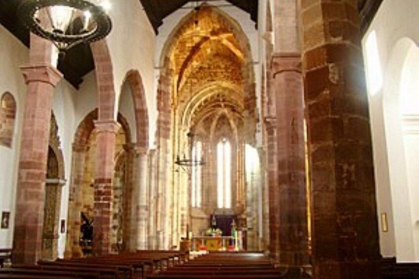 An interior of a cathedral with arched ceilings, stained glass windows, and a central altar. 1