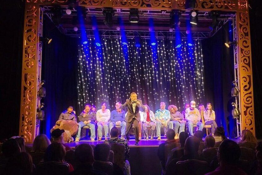 A stage with a group of people seated in a semi-circle, a central figure standing, and a backdrop of twinkling lights. 1