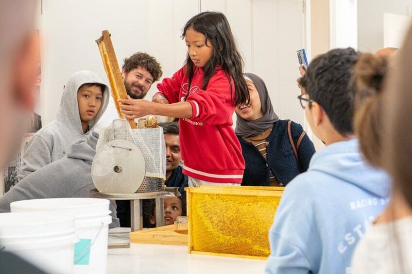 Een groep mensen neemt deel aan een interactieve activiteit, mogelijk een workshop of les, met verschillende gereedschappen en materialen op een tafel. 3