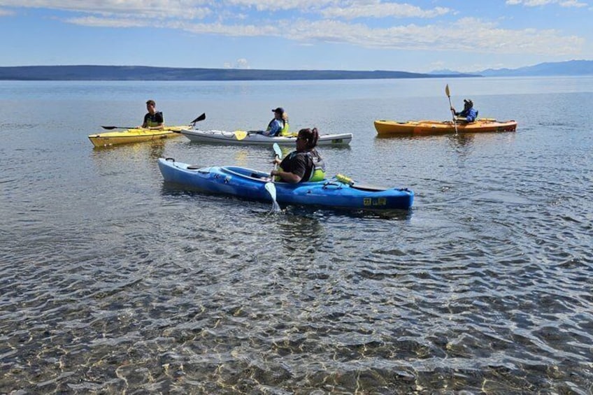People kayaking on a calm lake with clear water and distant mountains. 3