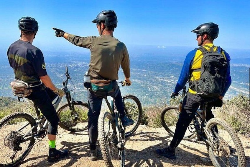 Tres ciclistas de montaña en un sendero con una vista panorámica de un valle. 1