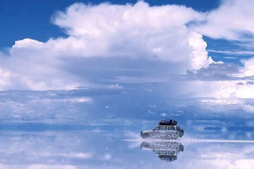 A car driving on a reflective surface with clouds in the sky. 2