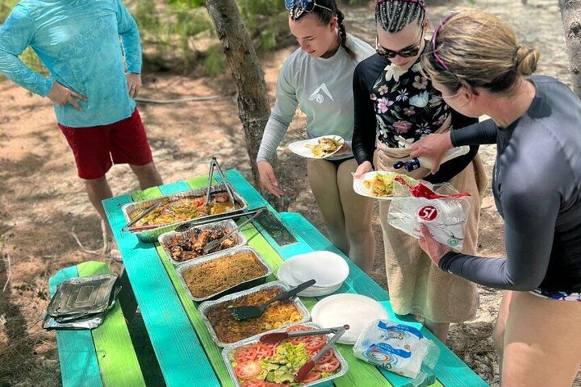 Un grupo de personas reunidas alrededor de una mesa de picnic con diferentes comidas. 1