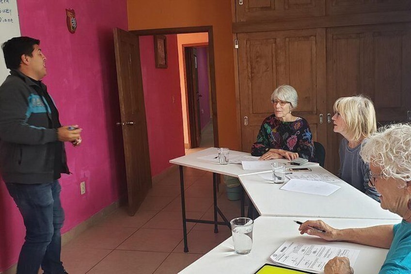A group of people in a room with a white table, wooden cabinets, and a pink wall. 1